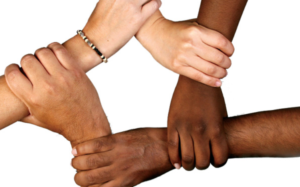 Five hands, all of different race/color, hold together.